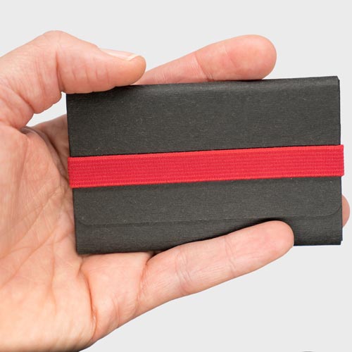 Kartenetui in der Hand haltend um die Größe der Kreditkarte zu erkennen. Das A&K TINY slim wallet ist Schwarz mit rotem Gummiband