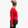 Black waist bag worn by a woman with a red sweater and black pants – casually styled on the strap or directly on the belt.