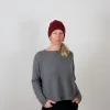 Portrait of a smiling woman wearing a burgundy beanie made of 100% merino wool, paired with a minimalist grey sweater against a light background.
