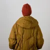 Rear view of a woman with a rust-red merino beanie and a metallic gold outdoor jacket for a modern winter look.